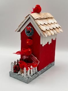 a red birdhouse with two birds sitting on it's roof