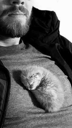 a man with a beard holding a cat in his lap and looking at the camera