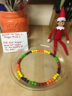 an elf is sitting on the counter next to a candy bead necklace and a note