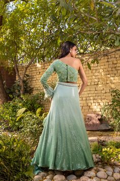 Radiate elegance in this exquisite green ombre lehenga set by Suruchi Parakh! Crafted from georgette crepe, this embellished ensemble exudes glamour with its intricate sequin work and delicate floral embroidery. The matching one-shoulder crop top features stunning feather detailing, perfectly complementing the organza ruffled dupatta. This masterpiece is a must-have addition to your ethnic wardrobe and sure to turn heads at any special occasion. Pista Green Sequined Georgette Lehenga, Floor-length Green Choli For Evening, Green Floor-length Choli For Evening, Green Floor-length Evening Choli, Elegant Pista Green Sequined Set, Green Floor-length Sharara For Evening, Festive Green Gown With Sequins, Fitted Pista Green Lehenga With Sequins, Glamorous Green Lehenga