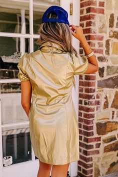 a woman standing in front of a brick building wearing a gold dress and blue hat