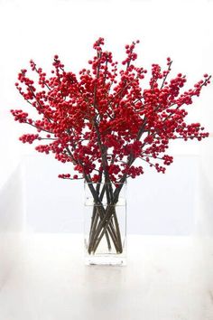 a vase filled with red flowers sitting on top of a white table next to a phone