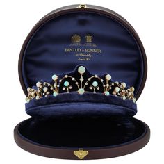 a blue velvet jewelry box with a gold crown on the top and pearls in it