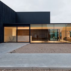 an empty building with glass walls and doors on the outside, in front of a gravel parking lot