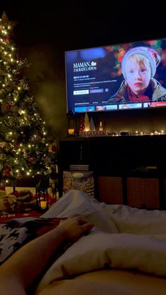 a person laying in bed with a christmas tree next to it and a large tv screen