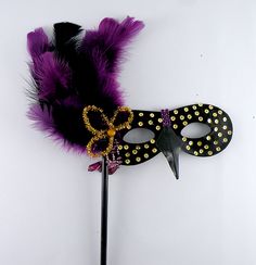 a masquerade mask with purple and black feathers on a white background, next to a pair of scissors