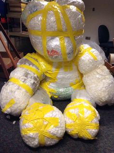 a large stuffed bear wrapped in plastic and sitting on the floor with yellow tape around it