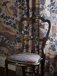 an ornate chair sits in front of a floral curtain