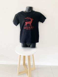 This cute black T shirt with red reindeer and merry and bright saying is the perfect T shirt for your little one on Christmas Day. Every detail of this design has been designed and created with care and attention, making this T shirt truly unique. From its vibrant, eye catching hue to the intricate reindeer graphic, this T shirt will add the perfect touch to your child's wardrobe. Australian size 5 The design is made from premium red glitter iron on vinyl and placed on a white cotton long sleeve T shirt. Please don't iron on the vinyl as it will melt and ruin the design. When washing please turn the T shirt inside out to preserve the design and don't put the T shirt in a dryer as this will also ruin the design. Black Christmas T-shirt As Gift, Black Crew Neck T-shirt For Holidays, Black Christmas T-shirt With Short Sleeves, Black Short Sleeve Christmas T-shirt, Holiday Black Short Sleeve Tops, Black Short Sleeve Holiday Tops, Christmas Black Graphic Tee T-shirt, Holiday Black T-shirt With Letter Print, Black Graphic Tee For Christmas