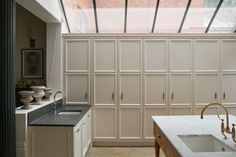 a kitchen with white cabinets and marble counter tops under a skylight above the sink