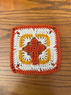 an orange and white crocheted square on top of a wooden table