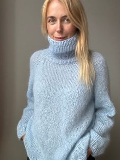 a blonde woman wearing a blue sweater and black pants is posing for the camera with her hands in her pockets