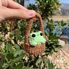 a hand holding a small crocheted bag with a green frog face on it