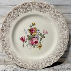 a white plate with pink and yellow flowers painted on the side, sitting on a marble countertop