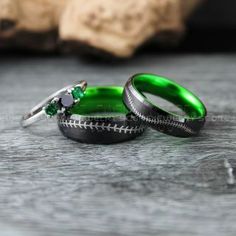 two wedding rings with green and white enamel inlays sitting on a wooden surface