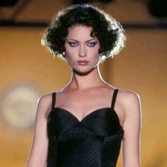 a woman in a black dress walking down a runway with her hand on her hip