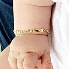 a close up of a person holding a baby's hand with a gold chain bracelet on it