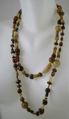 This necklace is 27 inches long allowing it to be worn3 different ways.  The colors are bronze, gold, brown, tan, copper, wood, pearls, etc.  It is a random and eclectic mix of like colored stones. There are pearls, wood, bamboo coral, Carnelian, Tiger Eye, Jade, and many many others, woven in harmony on 50 lb test nylon fishing cord.  There is no clasp. Brown Long Necklace In Costume Jewelry Style, Brown Costume Jewelry Necklace With Polished Beads, Brown Long Necklace With Natural Stones, Brown Polished Beads Costume Jewelry Necklace, Brown Long Costume Jewelry Necklace, Artisan Double Strand Brown Necklace, Brown Gemstone Beads Long Necklace, Brown Polished Beads Costume Necklace, Brown Gemstone Beaded Long Necklace