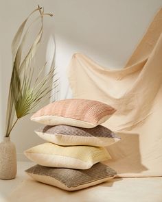 four pillows stacked on top of each other next to a vase with a plant in it