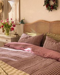 a bed with plaid sheets and pillows next to a wreath on the wall above it