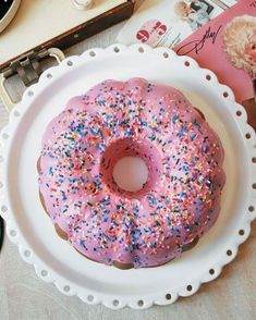 a pink frosted donut with sprinkles sits on a white plate