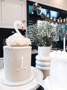 two white wedding cakes with swans on top and flowers in vases next to them