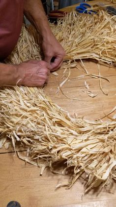 a man making a wreath out of straw on top of a wooden table next to a pair of scissors