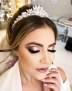 a woman wearing a tiara and makeup looks down at her finger on her lips