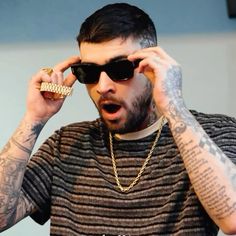 a man with tattoos on his arm and wearing sunglasses holding a chain to his face