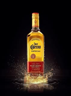 a bottle of liquor is splashing out of the water on a black background with gold flecks