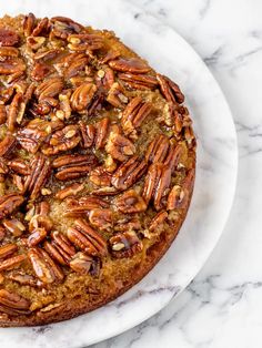 a cake with pecans on top is sitting on a white plate next to a marble counter