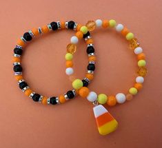 two beaded bracelets with candy corn on them and an orange, white, and black pendant