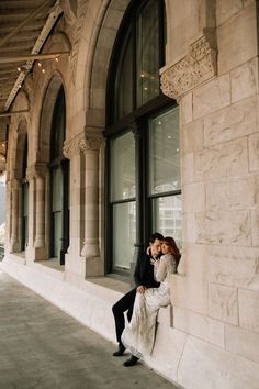 a man and woman leaning against a wall in front of a building with large windows