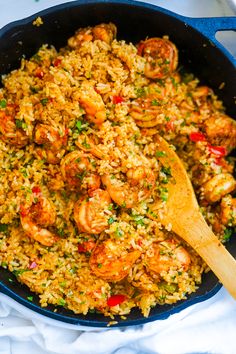 a skillet filled with shrimp and rice on top of a white cloth next to a wooden spoon