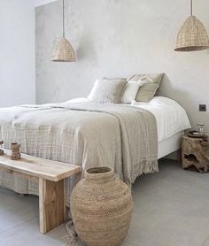 a bedroom with white walls and flooring, two hanging lights above the headboard