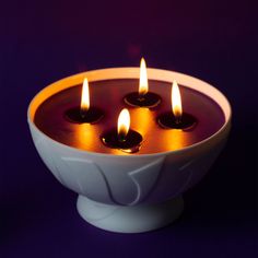 four lit candles in a white bowl on a purple background