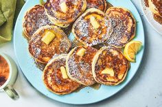 pancakes with powdered sugar and sliced lemons on a blue plate next to two cups of tea