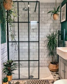 a bathroom with green walls and white tiles on the shower wall, plants in potted planters