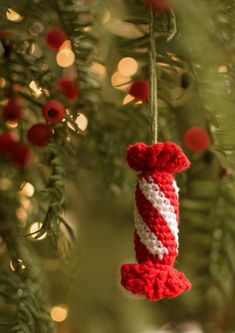 a red and white knitted ornament hanging from a christmas tree with lights in the background