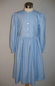 "Custom Girl's Prairie Dress A popular, simple dress for either a costume or everyday wear with a natural waist, gathered at the shoulder elbow length sleeves with narrow cuffs and a long, full skirt. This dress works well for everything from the late 1800's Little House look to the early 1900's. For winter, it is also available with long sleeves that end with slip over cuffs. The bodice buttons down the front and the full skirt is gathered at the waist. If you would like a longer than standard Classic Dress With Smocked Cuffs, Classic Fitted Dress With Smocked Cuffs, Classic Cotton Prairie Dress For Daywear, Cotton Prairie Dress For Daywear, Classic Fitted Long Sleeve Prairie Dress, Fitted Peasant Dress For Daywear, Fitted Peasant Dress With Puff Sleeves For Daywear, Cotton Long Sleeve Prairie Dress, Fitted Peasant Dress With Smocked Cuffs