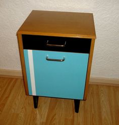 a small blue and black cabinet sitting on top of a hard wood floor next to a white wall