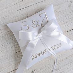 a white wedding ring pillow with the initials and date on it, tied to a wooden floor