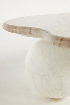 a white marble coffee table with an oval base and wooden top, on a plain surface