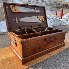 an old wooden chest with two knives in it on the ground next to some snow