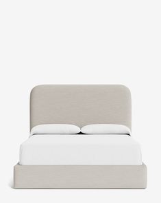 an upholstered bed with white sheets and pillows