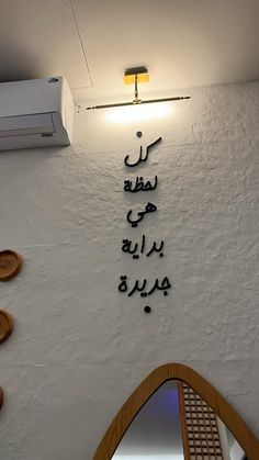 arabic writing on the wall above a mirror in a room with white walls and wood accents