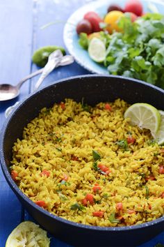 a pan filled with rice and vegetables on top of a blue table next to a salad