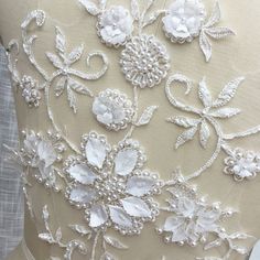 the back of a dress with white flowers and pearls on it's neckline