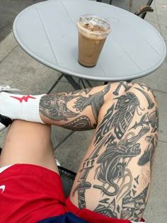 a man with tattoos on his legs sitting in front of a table next to a drink