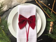 a white plate topped with a red bow tie on top of a napkin next to pine branches